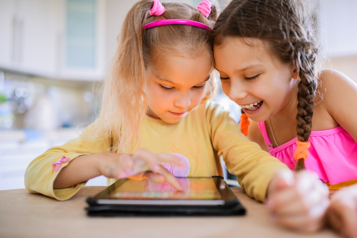 two children are using a tablet, one is scrolling, while the other is watching with a smile