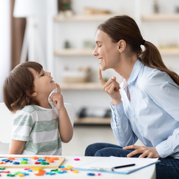 An adult women and a little girl smile at each other while each touching their chins in a speech exercise.