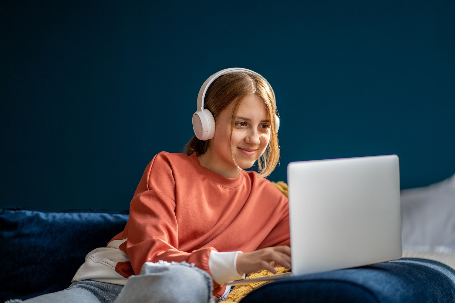 A young woman uses a laptop while wearing headphones.