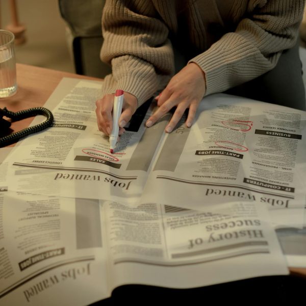 A person looks in a newspaper for job listings and circles some postings with a sharpie.