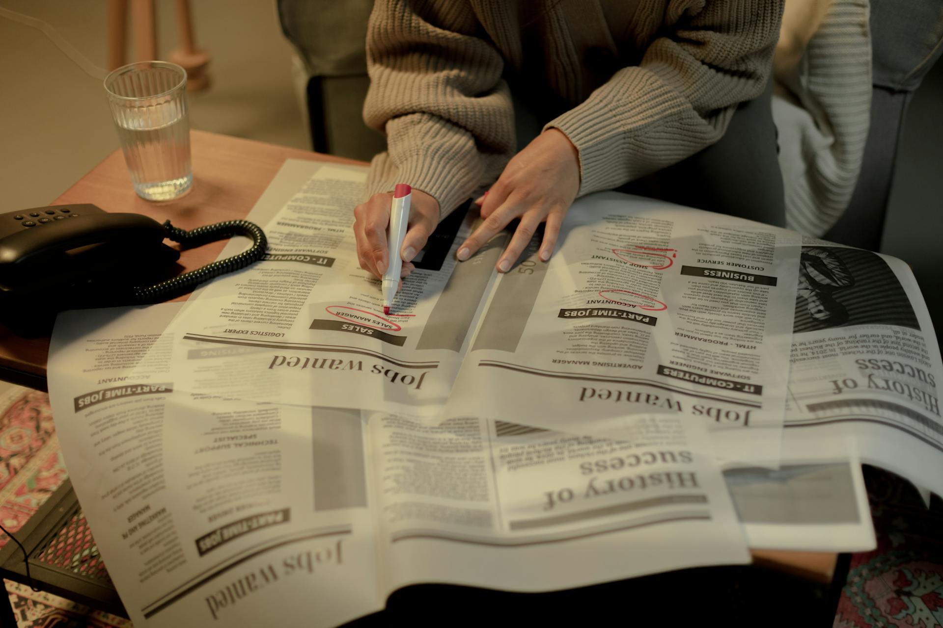 A person looks in a newspaper for job listings and circles some postings with a sharpie.