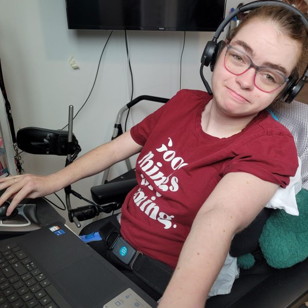 Hailey, in her wheelchair, at her desk using a trackball mouse and wearing a headset.