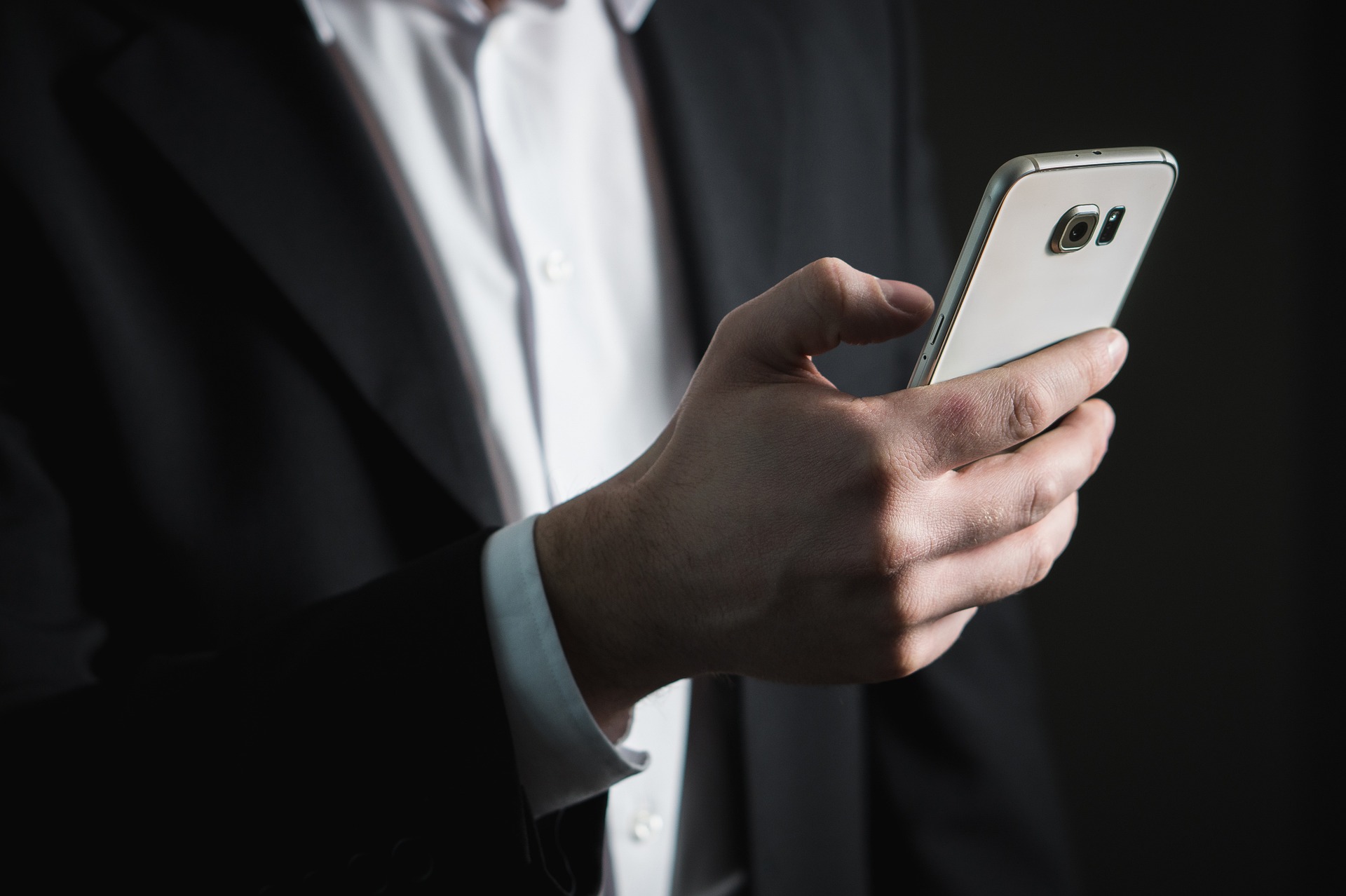 A man in a business suit browses his smartphone.