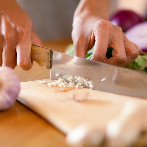 A chef finely chops garlic on a cutting board.