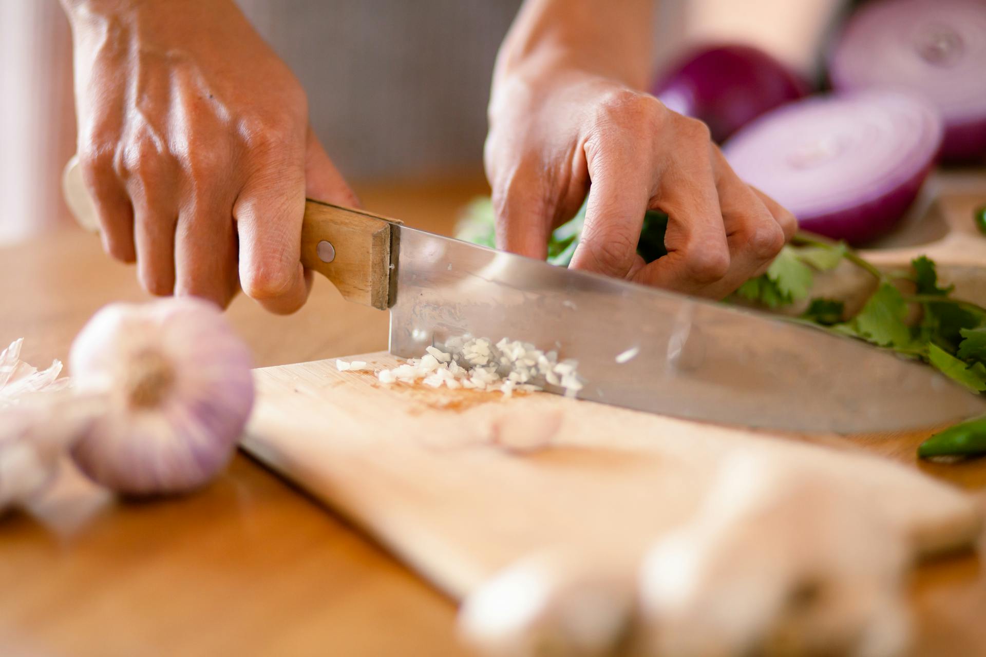 A chef finely chops garlic on a cutting board.