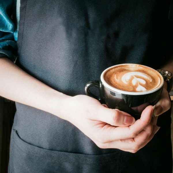 A barista holds a cup of cappuccino.