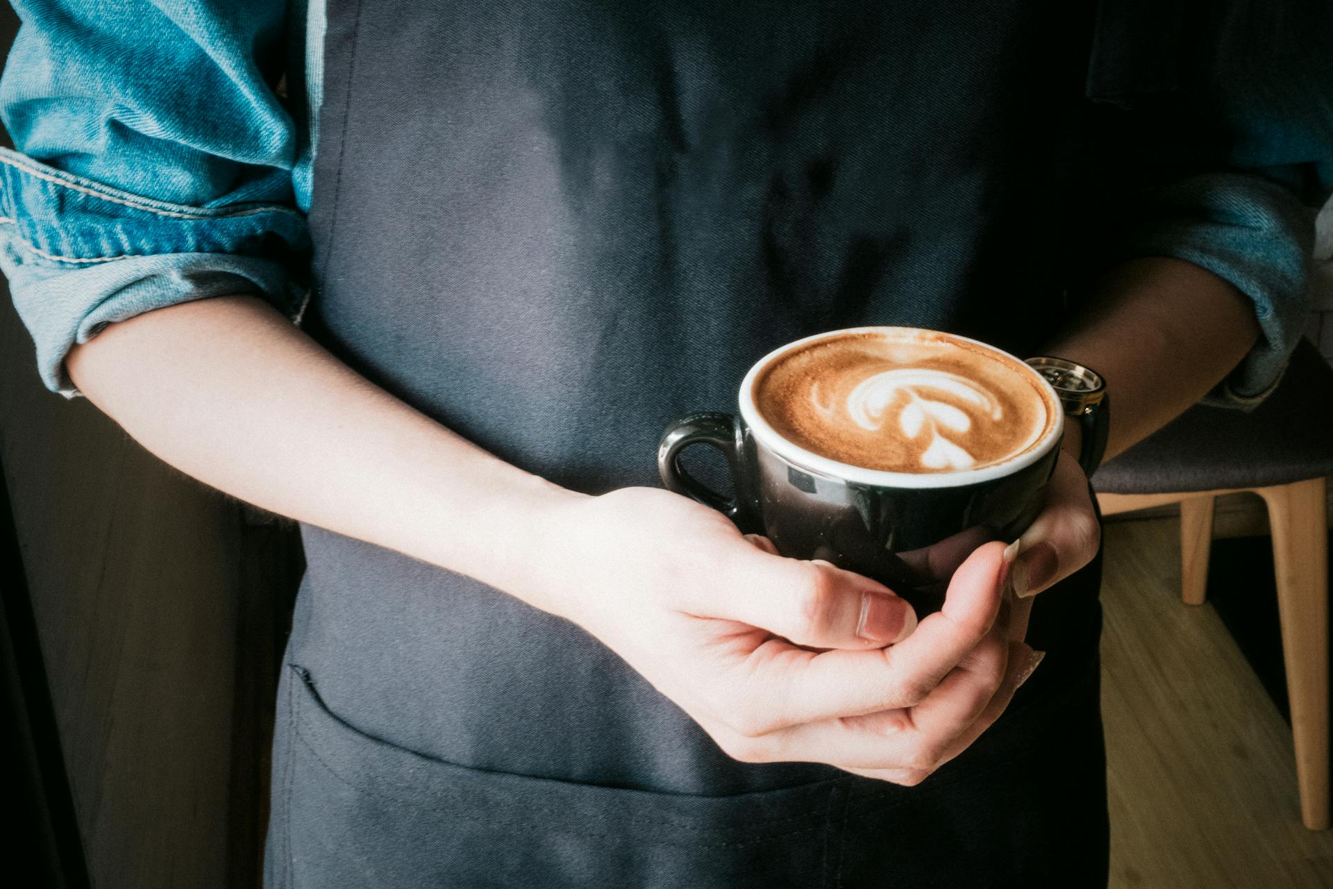 A barista holds a cup of cappuccino.