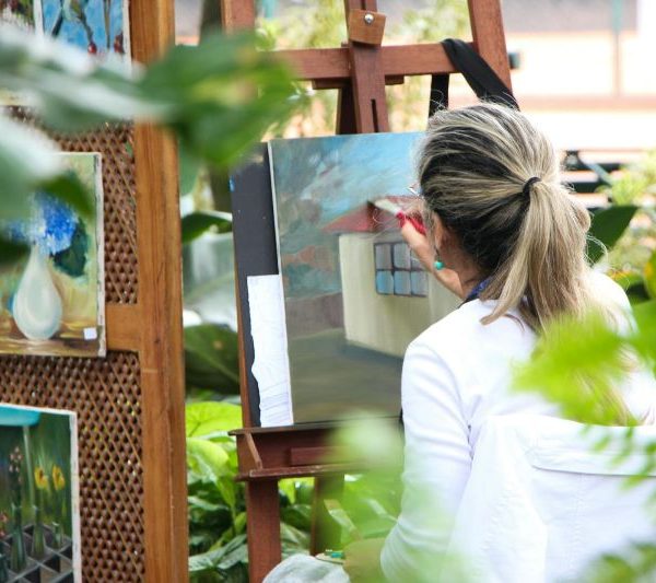 A woman paints on a canvas in a garden.