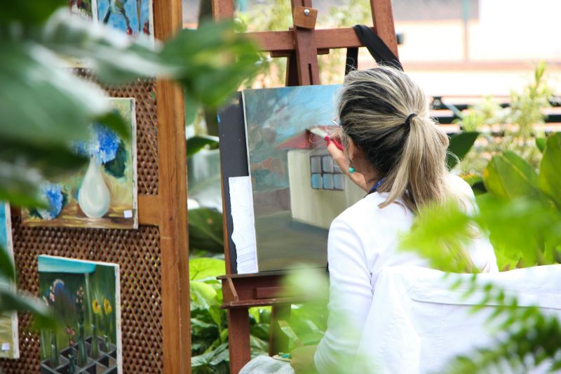 A woman paints on a canvas in a garden.