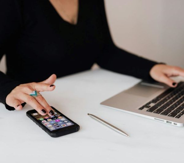 A woman uses her phone while using a laptop.