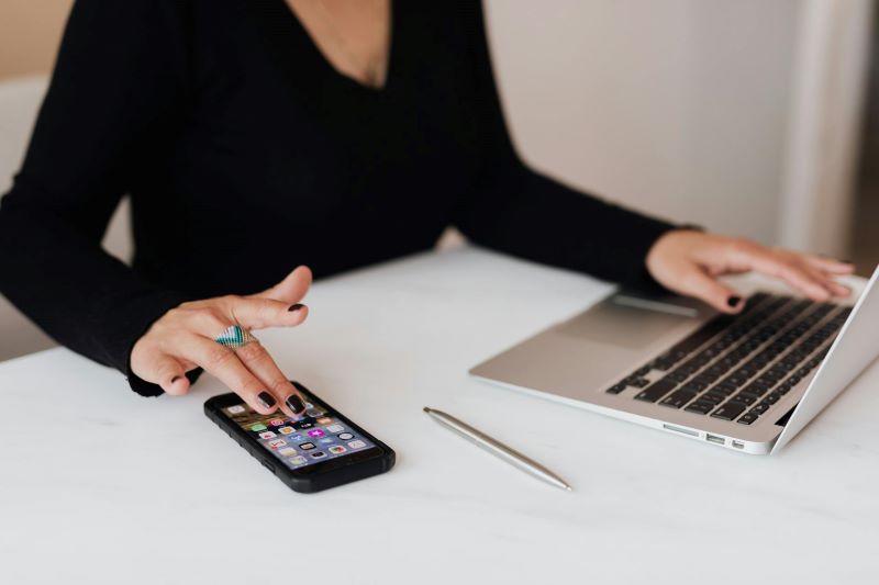 A woman uses her phone while using a laptop.