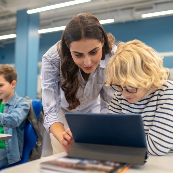 A teacher helps a student using a tablet.