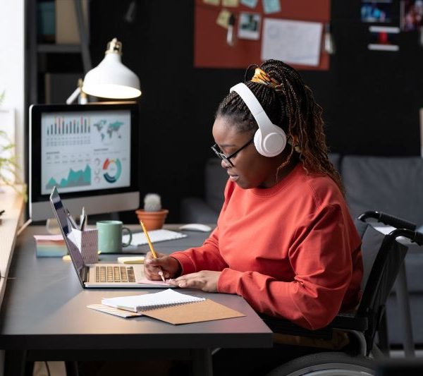 A young woman in a wheelchair takes down some notes while going on the computer