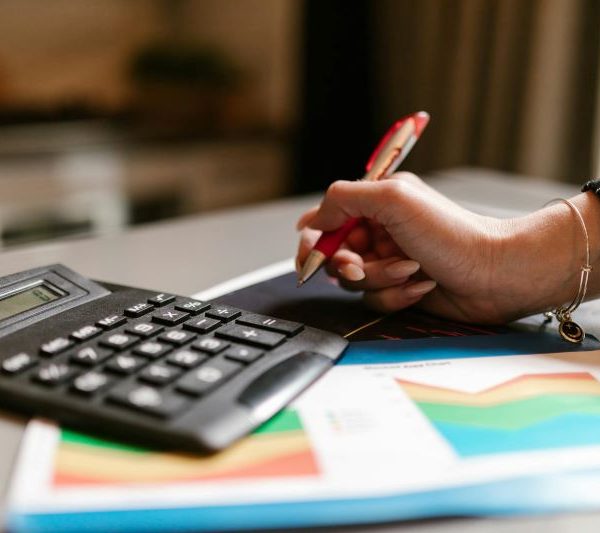 A woman holds a pen over some graphs next to a calculator