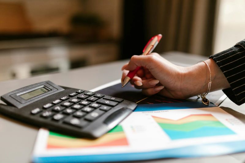 A woman holds a pen over some graphs next to a calculator