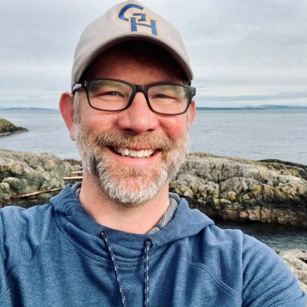 Ryan smiles in front of a rocky beach.