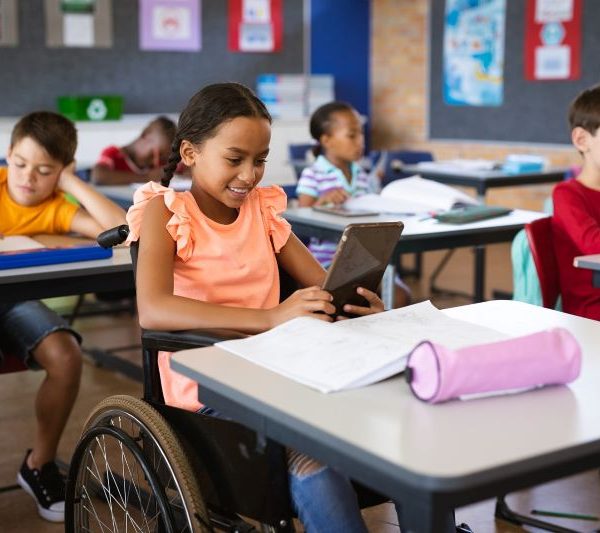 A girl in a wheelchair uses a tablet in class to do her homework.