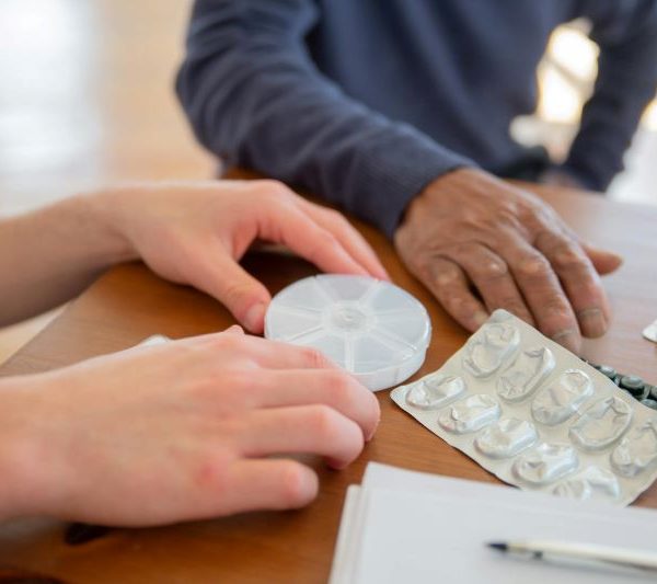 A health care worker helps an elderly man with his pills.