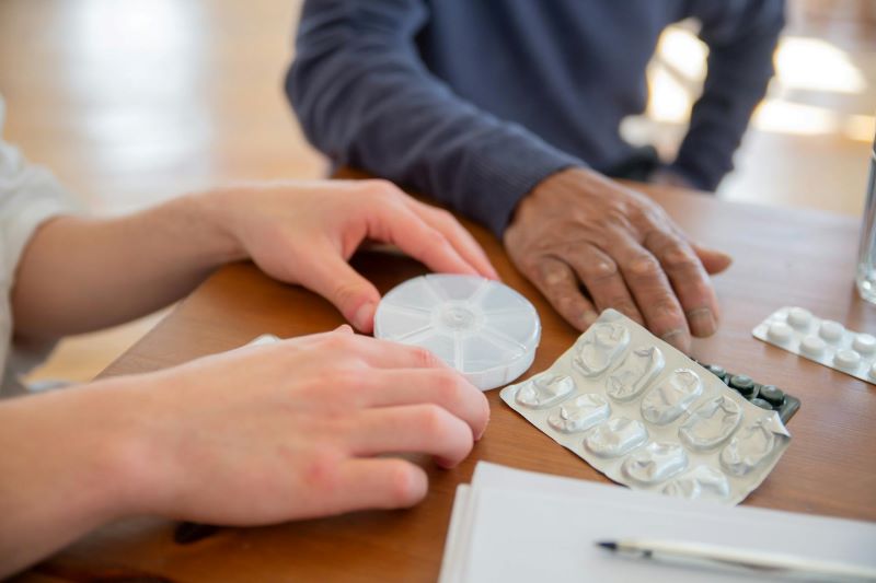 A health care worker helps an elderly man with his pills.