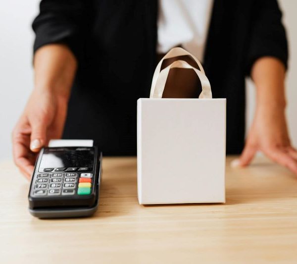 A woman passes over a payment terminal, while standing over a paper bag.