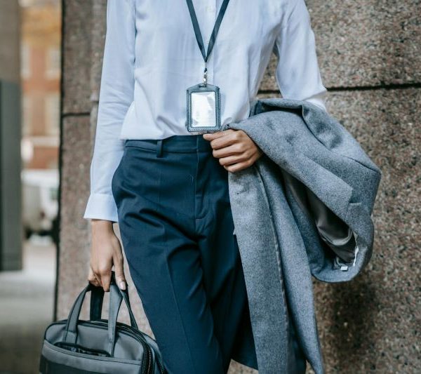 A woman holds her coat and briefcase in front of a building.