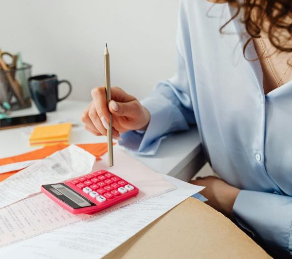 A woman looks over bills and uses a pencil to type on a calculator.