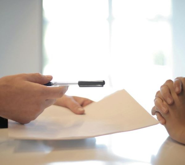 A man in a suit holding a pen and paper talks to a client.