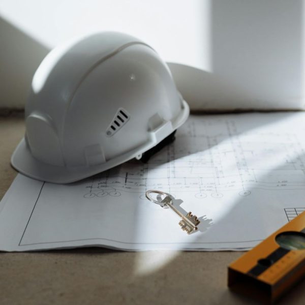 A hard hat sitting on a set of plans, along with keys and a level.