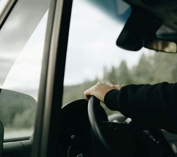 A person has their hand on the steering wheel as they drive.